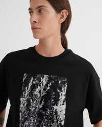 Person wearing a black t-shirt with a graphic design on a plain background
