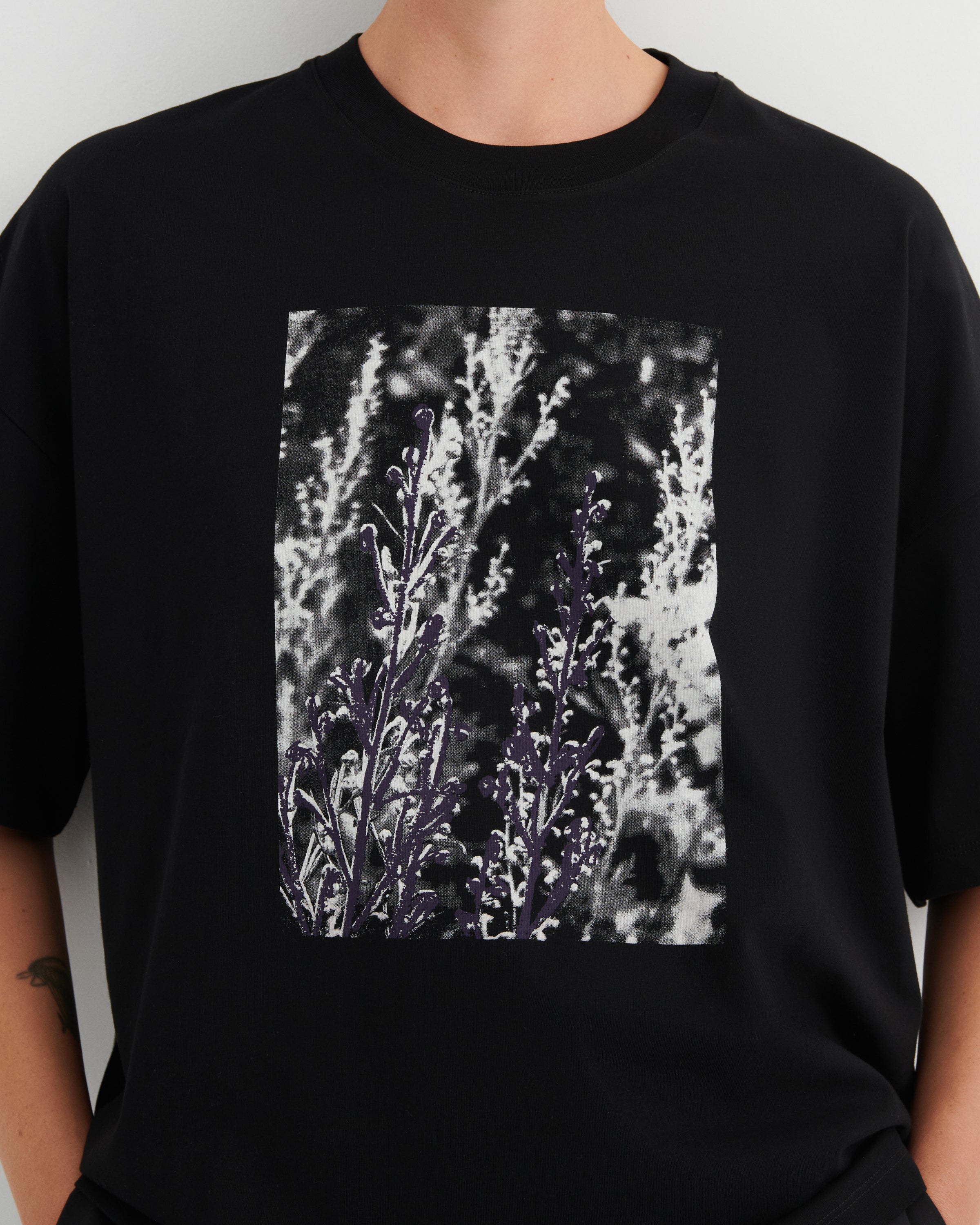 Black t-shirt with a graphic of purple flowers on a plain background