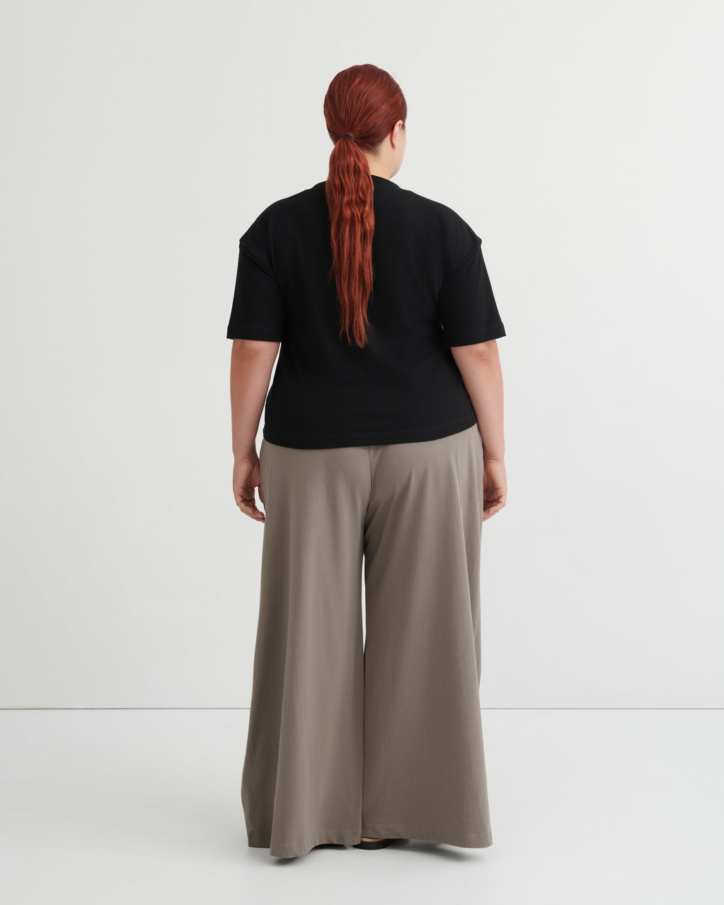 Person wearing a black top and beige pants on a white background