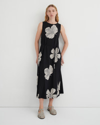 A woman modeling a sleeveless black midi dress with a large gray floral print, standing against a plain white studio background.