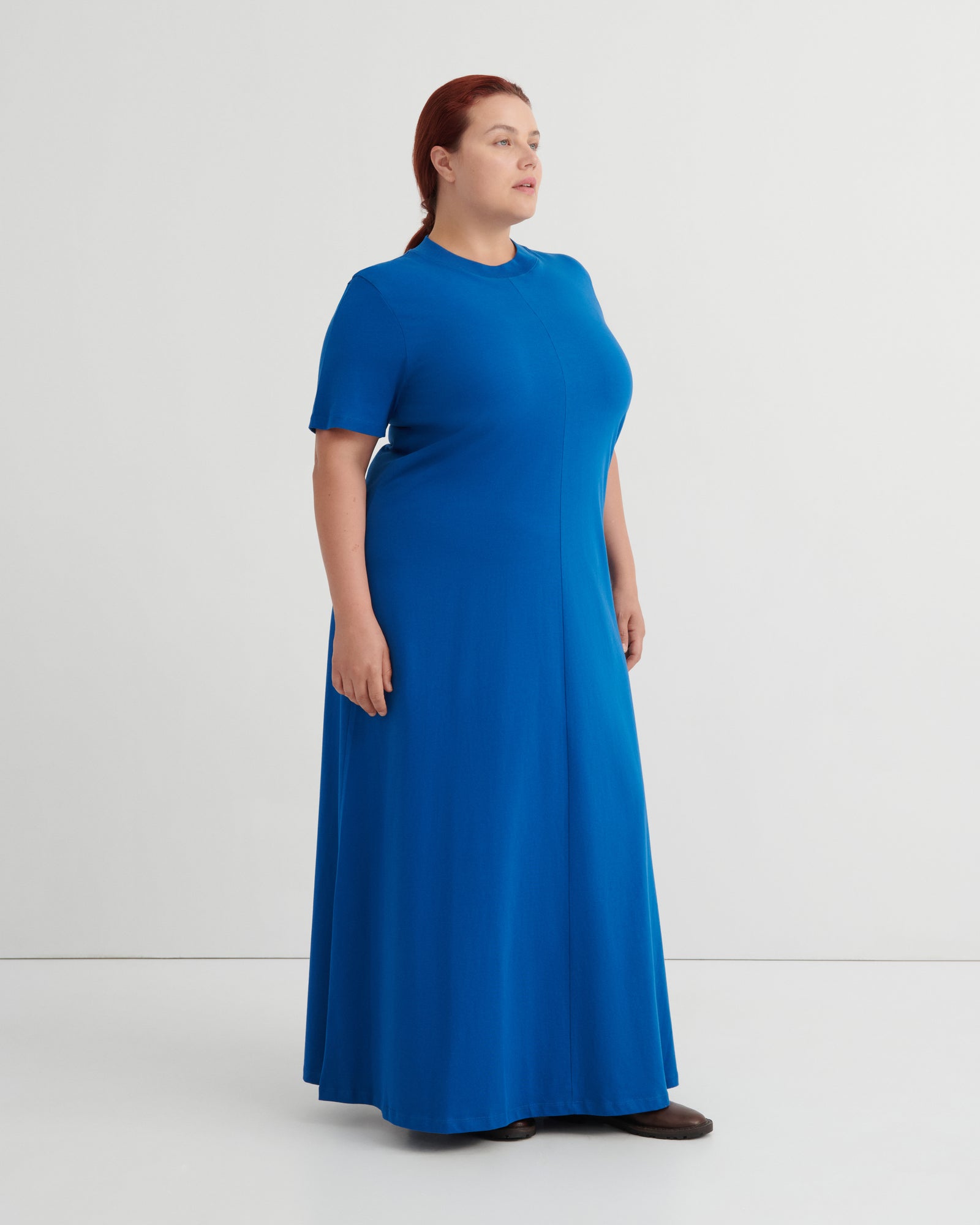 A woman modeling a bright blue short-sleeve maxi dress against a plain light gray studio background.