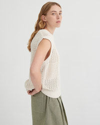 Woman wearing a white knitted vest and green pants on a light gray background