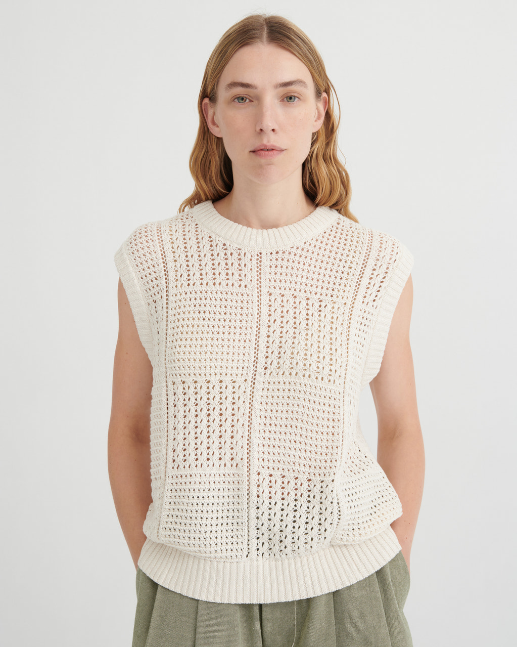 Woman wearing a white sleeveless knitted top against a plain background
