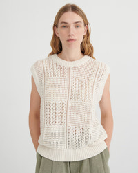 Woman wearing a white sleeveless knitted top against a plain background