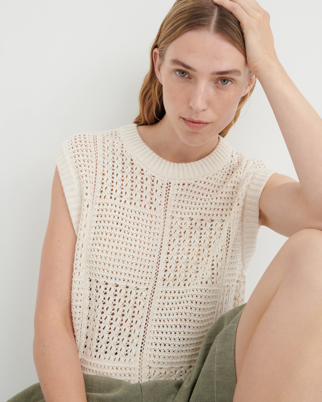 Woman wearing a beige sleeveless crochet top against a white background
